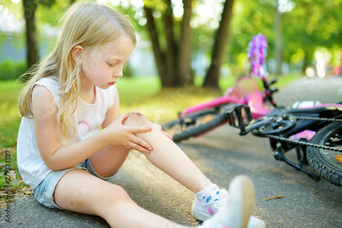 Fotografie Cute little girl sitting on the ground after falling off her bike at summer park
