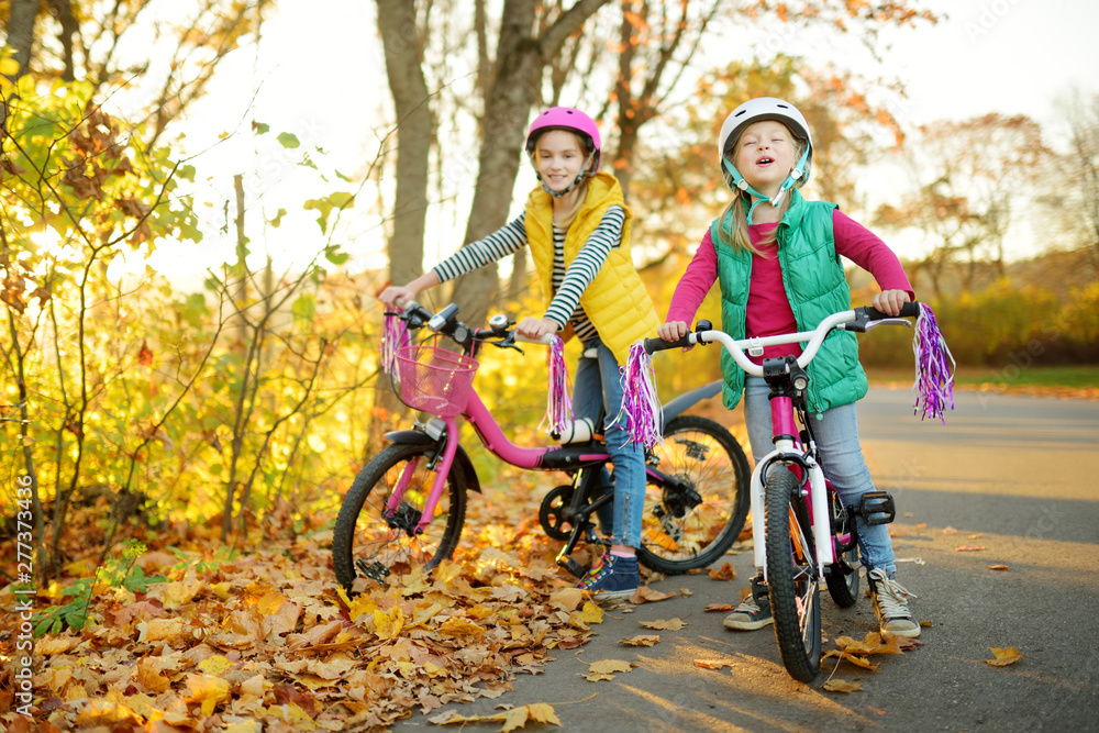 Cute little sisters riding bikes in a city park on sunny autumn day. Active family leisure with kids.