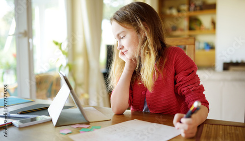 Fotografi Smart preteen schoolgirl doing her homework with digital tablet at home