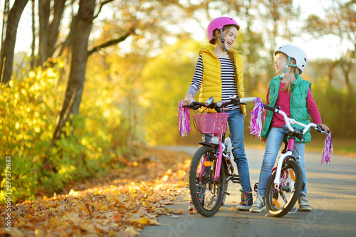 Cute little sisters riding bikes in a city park on sunny autumn day. Active family leisure with kids.