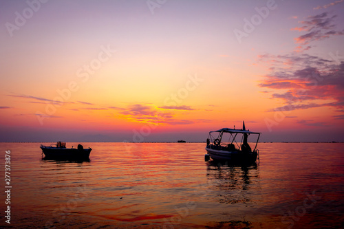 Silhouetted shot of beautiful sunrise with fisherman boat on the water