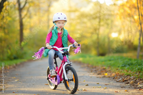Cute little girl riding a bike in a city park on sunny autumn day. Active family leisure with kids.