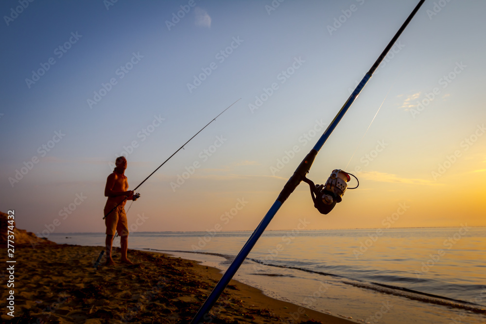 Man is fishing with several rods on the beach in sunrise morning