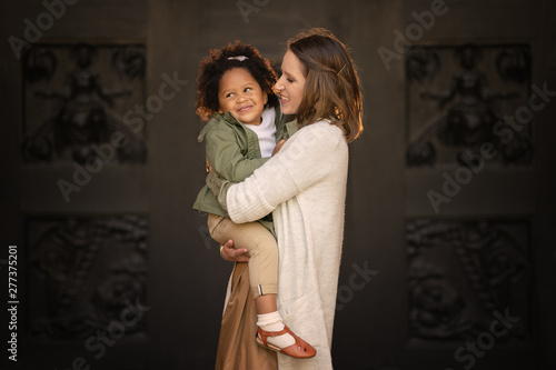 happy caucasian mother holding african american daughter on the hands