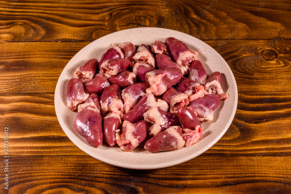 Ceramic plate with raw chicken hearts on wooden table