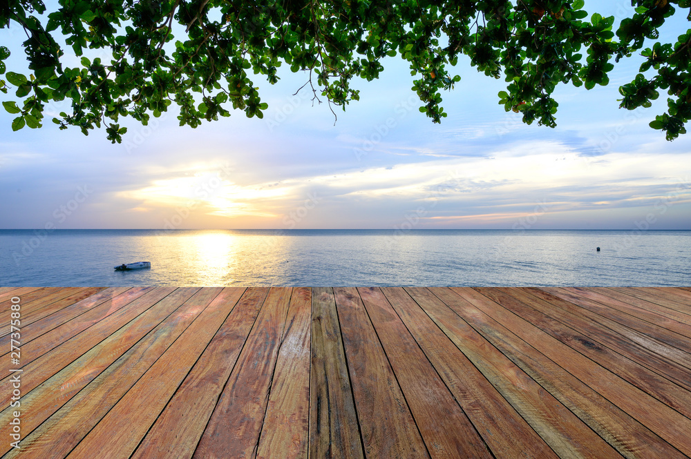 Empty wooden pier on sea coast and green leaves over head on tropical beach sunset on background