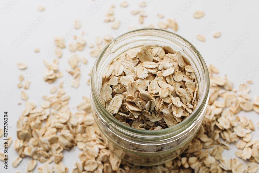 Jar and scatterd raw oat-flakes on white background Jar and scatterd raw oat-flakes on white background