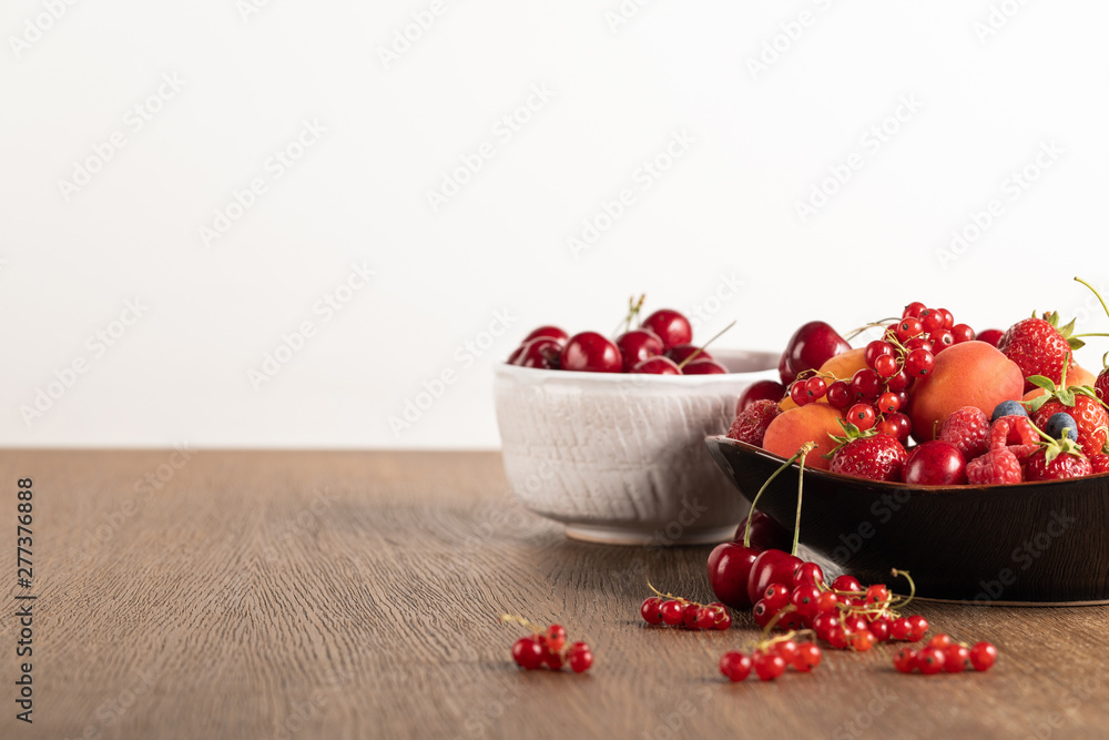 selective focus of cherries in white bowl and mixed berries on plate on wooden table isolated on white selective focus of cherries in white bowl and mixed berries on plate on wooden table isolated on white