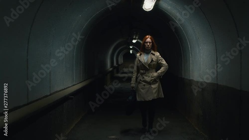 Following front view shot of businesswoman in a coat going through the tunnel in the evening and answering the mobile phone photo