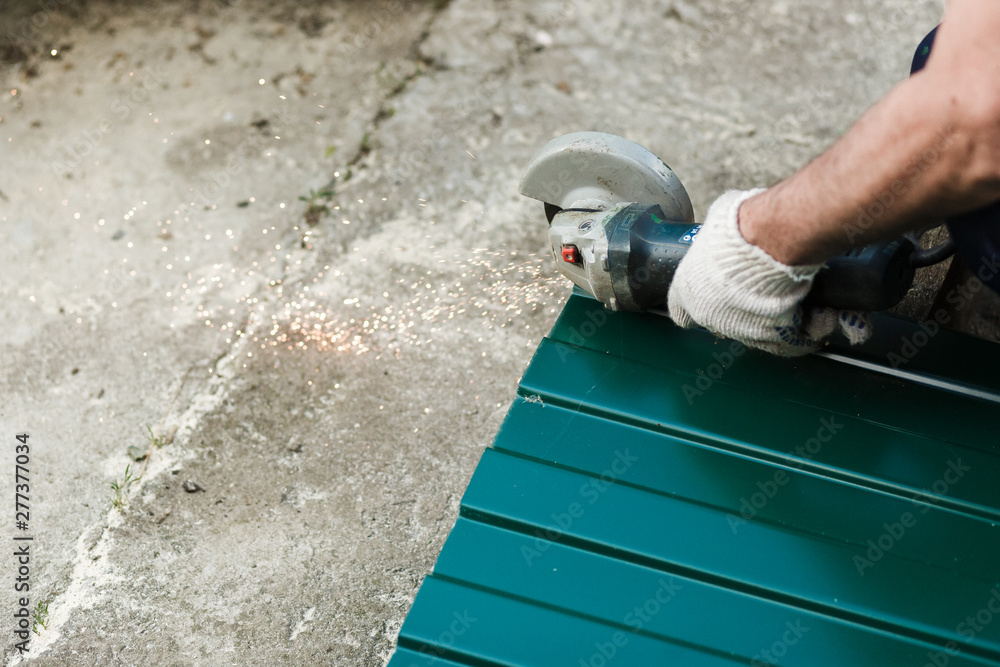 The master cuts a professional metal sheet for installation on the roof of the house. Roofer cutting metal roof sheets, metal tile for house roofing construction. The master cuts a professional metal sheet for installation on the roof of the house. Roofer cutting metal roof sheets, metal tile for house roofing construction.