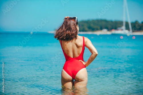 woman standing in sea in the middle in red swimming suit. view from behind. sexy ass © phpetrunina14