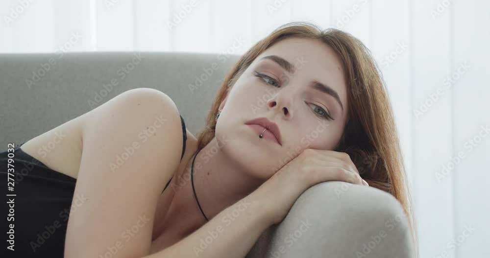 Closeup shoot of young seductive caucasian female in black bodysuit laying on the couch looking at camera indoors Closeup shoot of young seductive caucasian female in black bodysuit laying on the couch looking at camera indoors