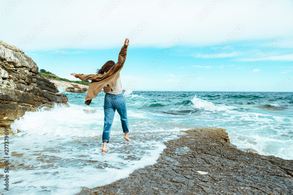 woman walking by rocky sea beach at sunny windy day. summer vacation