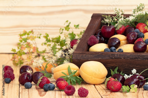 wooden box with fresh summer berries and fruits. Blueberries, cherry, strawberries, raspberries, apricots, forest flowers and herbs on a wooden table in a rustic style