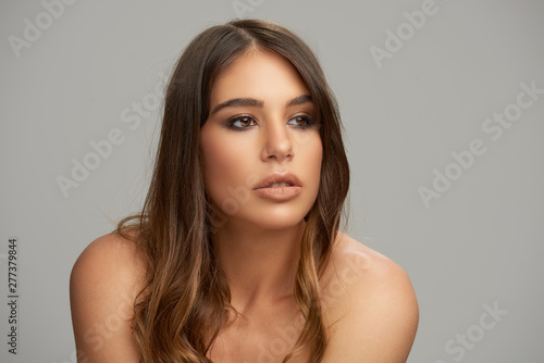 Headshot of beautiful Caucasian brunette posing in front of grey background. Beauty photography.
