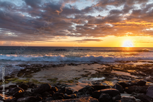 Dramatic sunset at the rocky beach with canoes in the background. Big Island Hawaii.