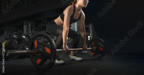 Determined and strong fitness woman training with heavy weights in fitness club. Female athlete holding heavy weight barbell in gym. Woman weightlifter preparing for training. Training with barbell