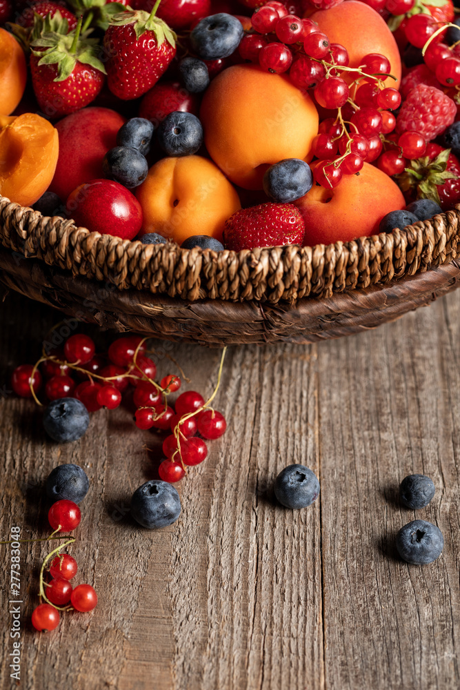 close up view of ripe berries and apricots in wicker basket on wooden table close up view of ripe berries and apricots in wicker basket on wooden table