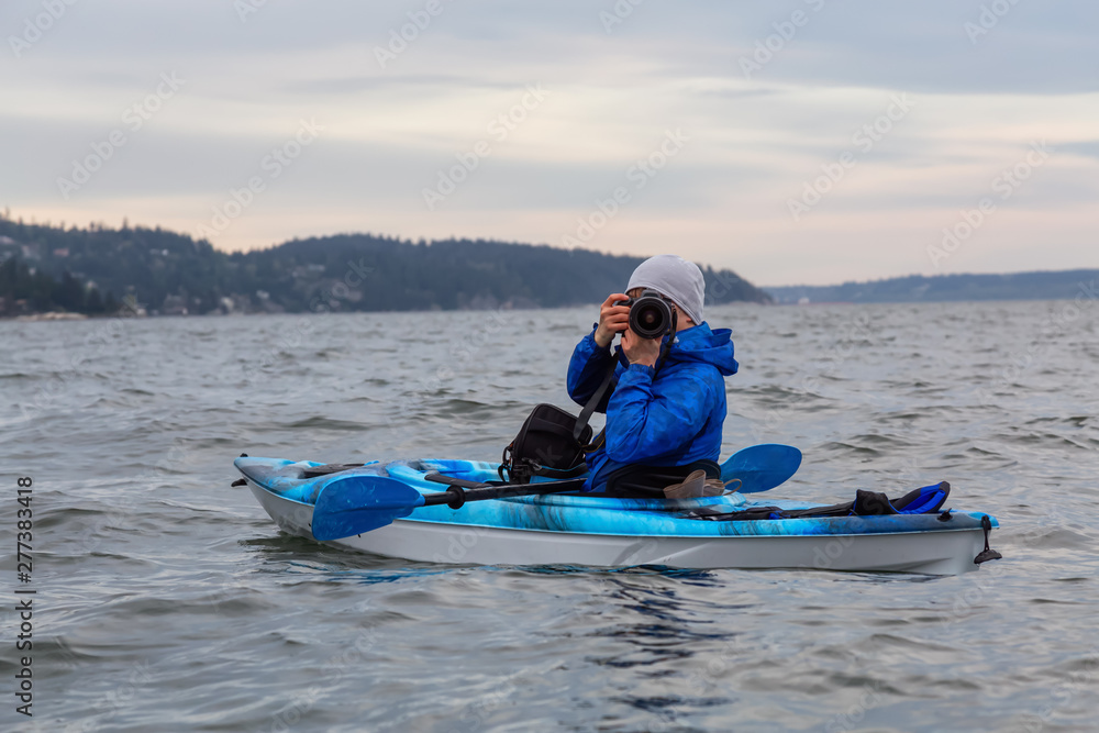 Naklejka premium Adventure photographer taking pictures with his camera from a kayak in the ocean. Taken in Howe Sound near Horseshoe Bay, West Vancouver, British Columbia, Canada.