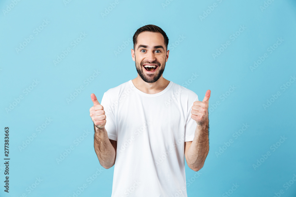 Excited young happy bearded man posing isolated over blue wall background showing thumbs up gesture. - obrazy, fototapety, plakaty 