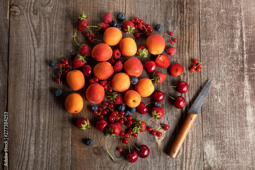 top view of ripe delicious fresh berries and apricots on wooden table with knife
