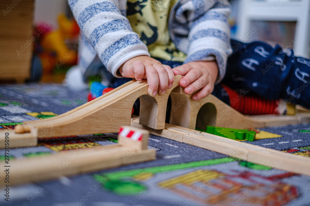baby hands playing with wooden train set on wooden rails on a carpet in nursery