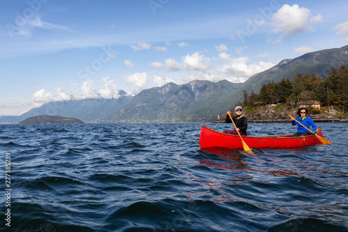 Couple adventurous female friends on a red canoe are paddling in the Howe Sound during a cloudy and sunny evening. Taken near Horseshoe Bay  West of Vancouver  BC  Canada.