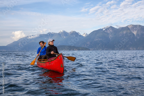 Couple adventurous female friends on a red canoe are paddling in the Howe Sound during a cloudy and sunny evening. Taken near Bowen Island, West of Vancouver, BC, Canada. © edb3_16