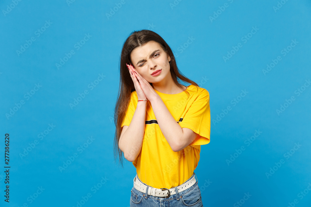 Portrait of displeased blinking young woman in vivid casual clothes sleeping with folded hands under cheek isolated on bright blue background in studio. People lifestyle concept. Mock up copy space. Portrait of displeased blinking young woman in vivid casual clothes sleeping with folded hands under cheek isolated on bright blue background in studio. People lifestyle concept. Mock up copy space.