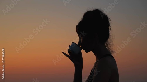 Close up side view of woman's silhouette who drinks tea enjoing of amazing sunrise view slow motion