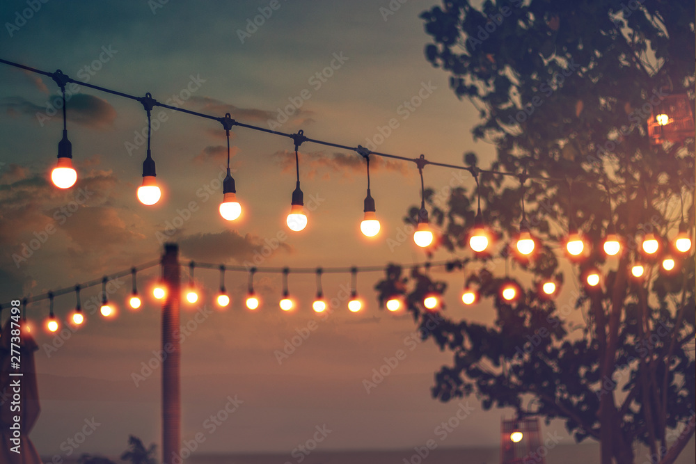 blurred bokeh light on sunset with yellow string lights decor in beach restaurant - obrazy, fototapety, plakaty 