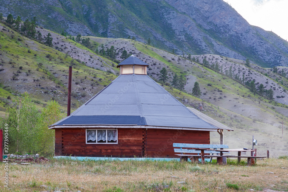 The ancient antique ail house from wood is round-shaped with a chimney on top of the center, for the nomadic indigenous people in the Altai Mountains with green trees and picturesque scenery.