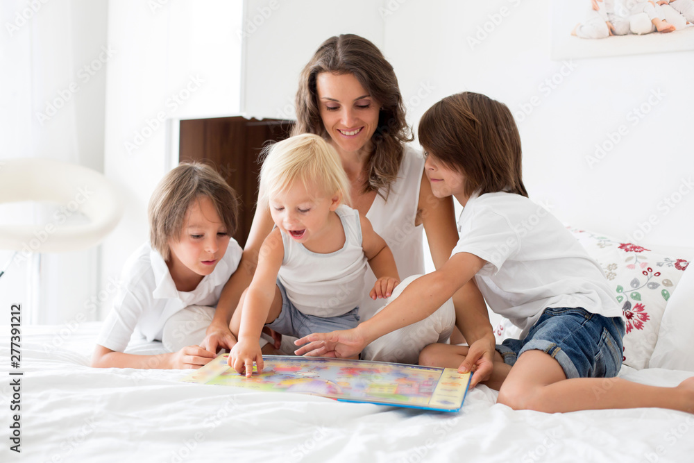 Young mother, read a book to her three children, boys, in the bed Young mother, read a book to her three children, boys, in the bed
