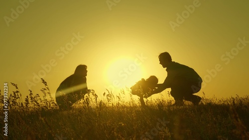 Little daughter with parents jumping at sunset. Silhouettes of mom dad and baby in the rays of dawn. Family concept. Walking with a small child in nature