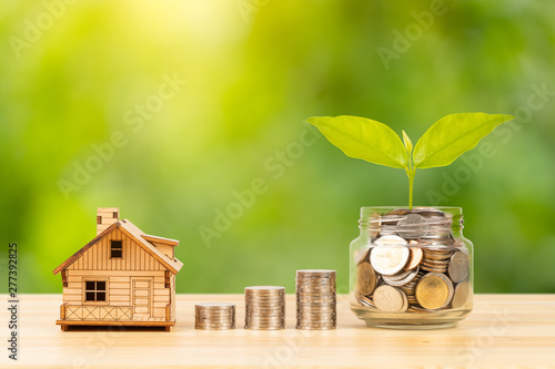 Coin jar and stack, and model house on wooden desk on green tree background, mortgage concept photo