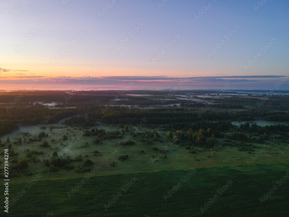 Obraz premium View from the height of the quadcopter on the landscape before dawn , fog dissipates in the fields near the forest.