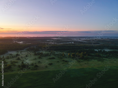 View from the height of the quadcopter on the landscape before dawn , fog dissipates in the fields near the forest.