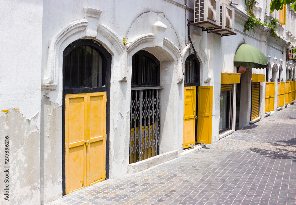 Empty sidewalk near a wall historic colonial-style building with wooden shutters and bars on windows on a hot sunny day in the old district of Kuala Lumpur, Malaysia