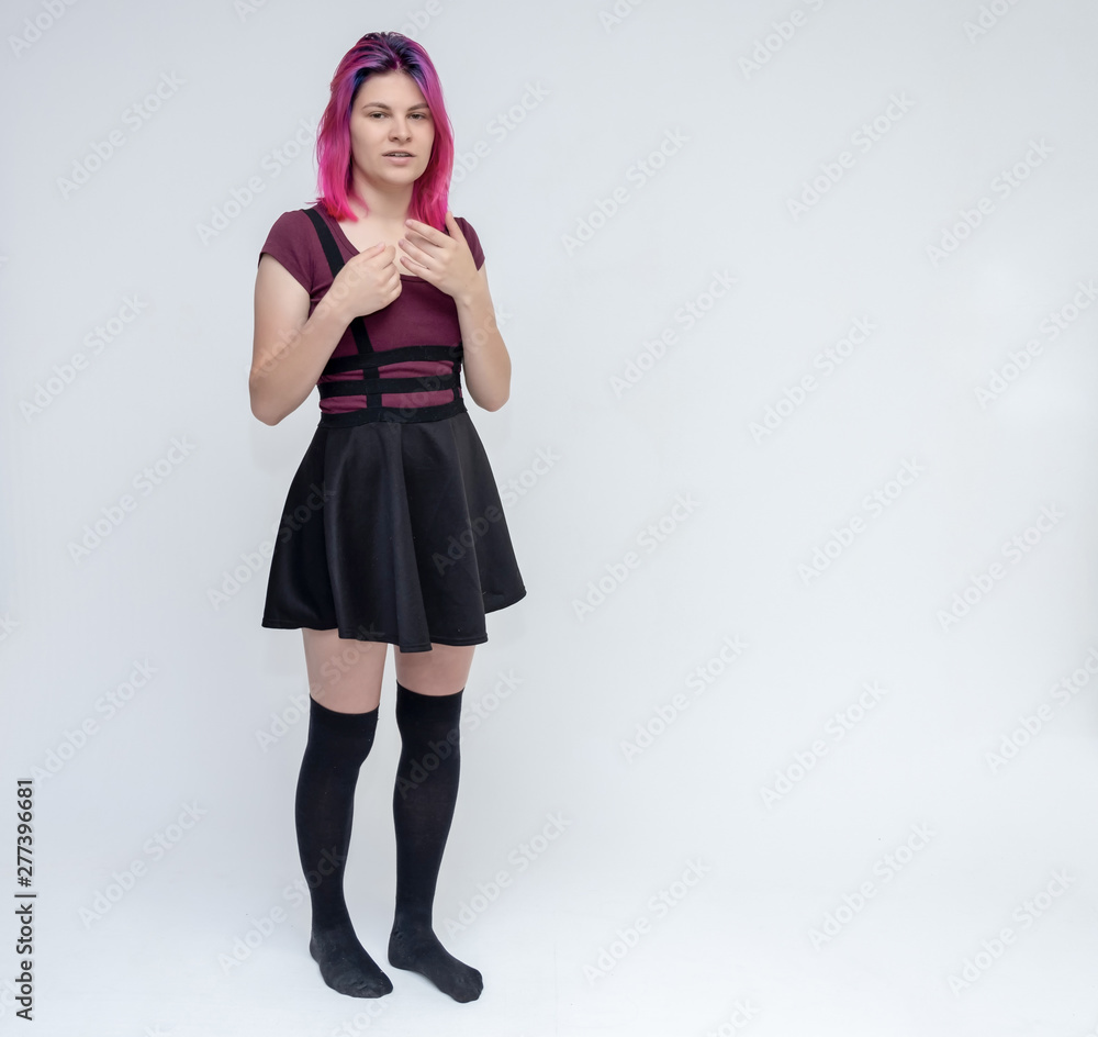 Full-length portrait of young pretty teenager girl in burgundy T-shirt and black dress with beautiful purple hair on a white background in the studio. Talking, smiling, showing hands with emotions. Full-length portrait of young pretty teenager girl in burgundy T-shirt and black dress with beautiful purple hair on a white background in the studio. Talking, smiling, showing hands with emotions.