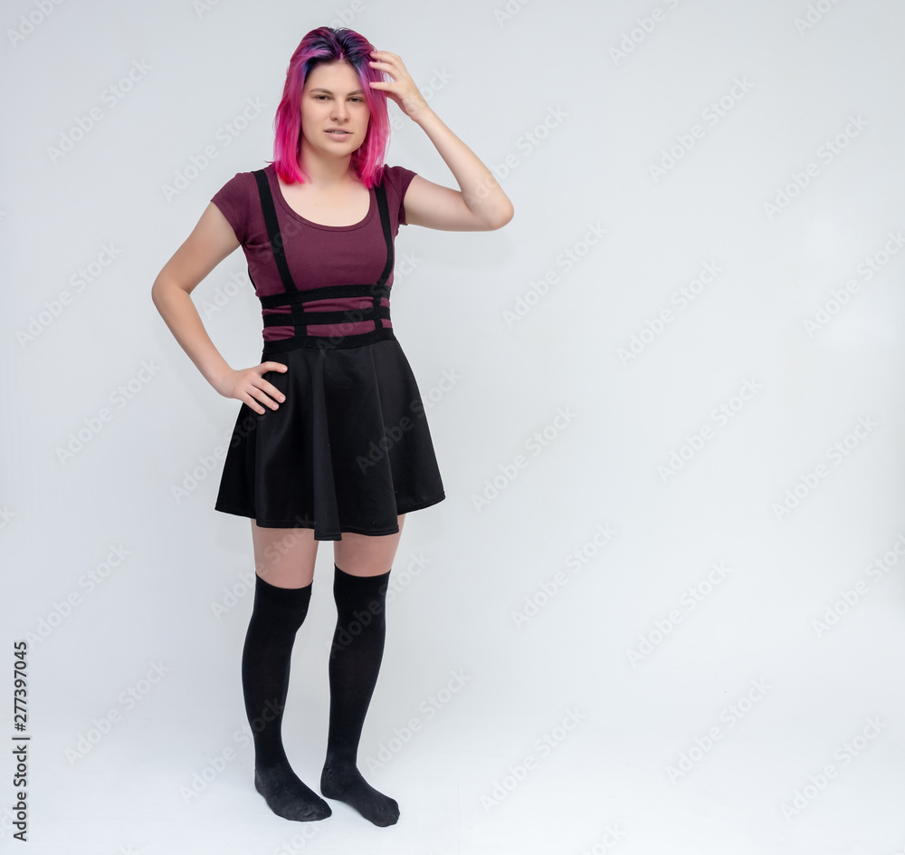 Full-length portrait of young pretty teenager girl in burgundy T-shirt and black dress with beautiful purple hair on a white background in the studio. Talking, smiling, showing hands with emotions. Full-length portrait of young pretty teenager girl in burgundy T-shirt and black dress with beautiful purple hair on a white background in the studio. Talking, smiling, showing hands with emotions.