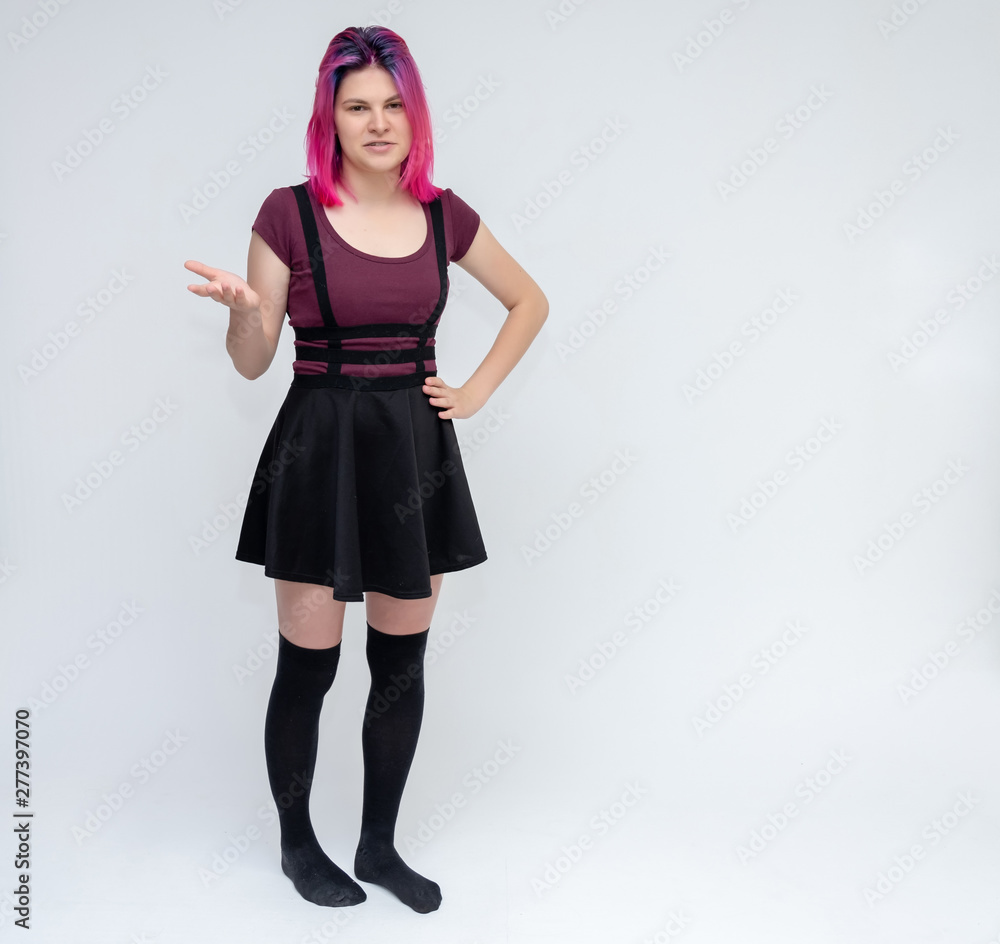 Full-length portrait of young pretty teenager girl in burgundy T-shirt and black dress with beautiful purple hair on a white background in the studio. Talking, smiling, showing hands with emotions. Full-length portrait of young pretty teenager girl in burgundy T-shirt and black dress with beautiful purple hair on a white background in the studio. Talking, smiling, showing hands with emotions.