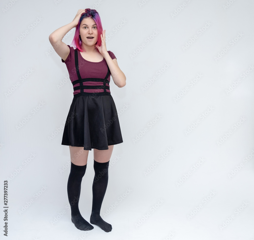 Full-length portrait of young pretty teenager girl in burgundy T-shirt and black dress with beautiful purple hair on a white background in the studio. Talking, smiling, showing hands with emotions. Full-length portrait of young pretty teenager girl in burgundy T-shirt and black dress with beautiful purple hair on a white background in the studio. Talking, smiling, showing hands with emotions.