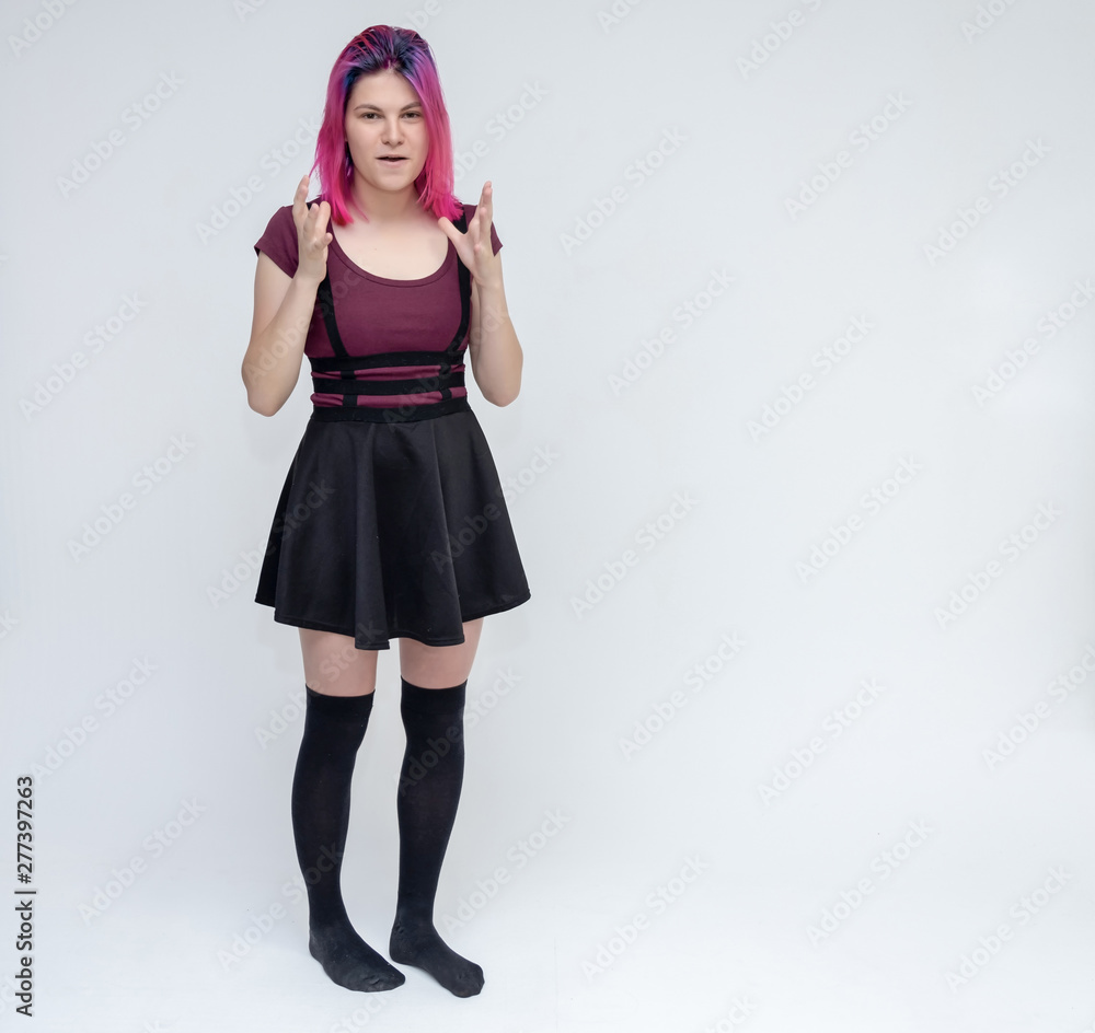 Full-length portrait of young pretty teenager girl in burgundy T-shirt and black dress with beautiful purple hair on a white background in the studio. Talking, smiling, showing hands with emotions. Full-length portrait of young pretty teenager girl in burgundy T-shirt and black dress with beautiful purple hair on a white background in the studio. Talking, smiling, showing hands with emotions.