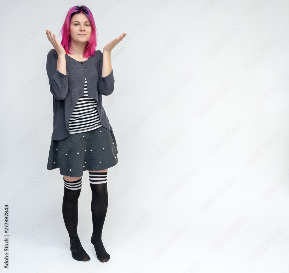 Obraz premium Full-length portrait of young pretty teenager girl in gray suit with beautiful purple hair on a white background in the studio. Talking, smiling, showing hands with emotions.