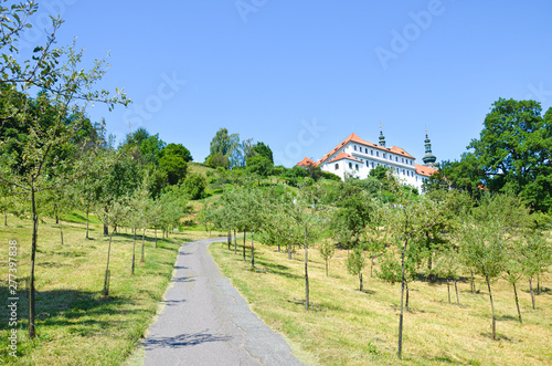 Stunning green gardens on Petrin Hill in the center of Prague, the Czech capital. Historical building with towers in background. Clear day, blue sky. Popular view point in the old town. City park