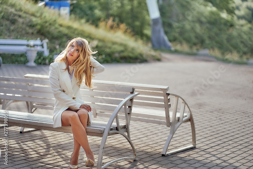 slim girl in a white coat sitting on a park bench. copy space photo