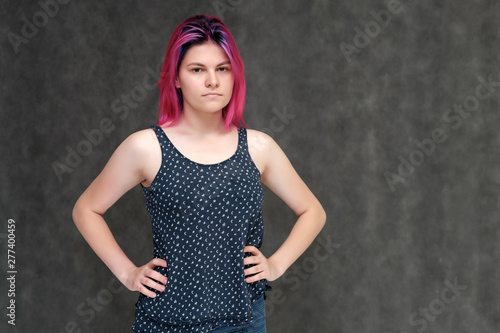 Portrait to the waist of a young pretty girl teenager in a T-shirt with beautiful purple hair on a gray background in the studio. Talking, smiling, showing hands with emotions.