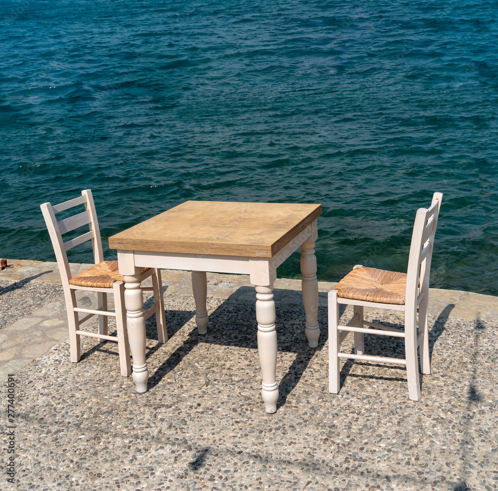 Ierapetra, Crete, Greece. June 2019. Table and two chairs set customer use on the quayside at this southern Crete resort. Ierapetra, Crete, Greece. June 2019. Table and two chairs set customer use on the quayside at this southern Crete resort.