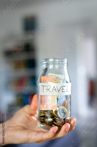 Mão a agarrar frasco de mealheiro etiquetado "Travel".