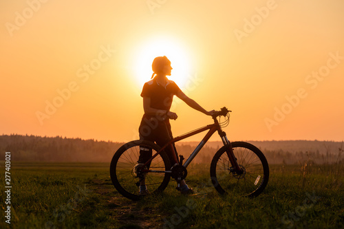 Happy girl with a bicycle on the nature on the background of bright sunset and yellow sun